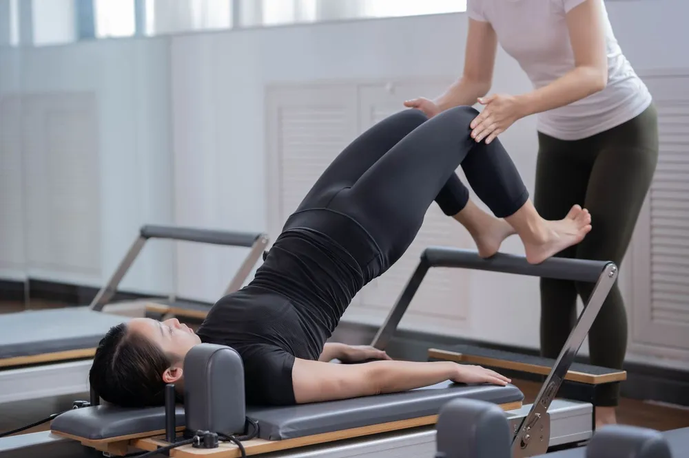 Profesora ajustando la postura de una alumna tumbada en el reformer